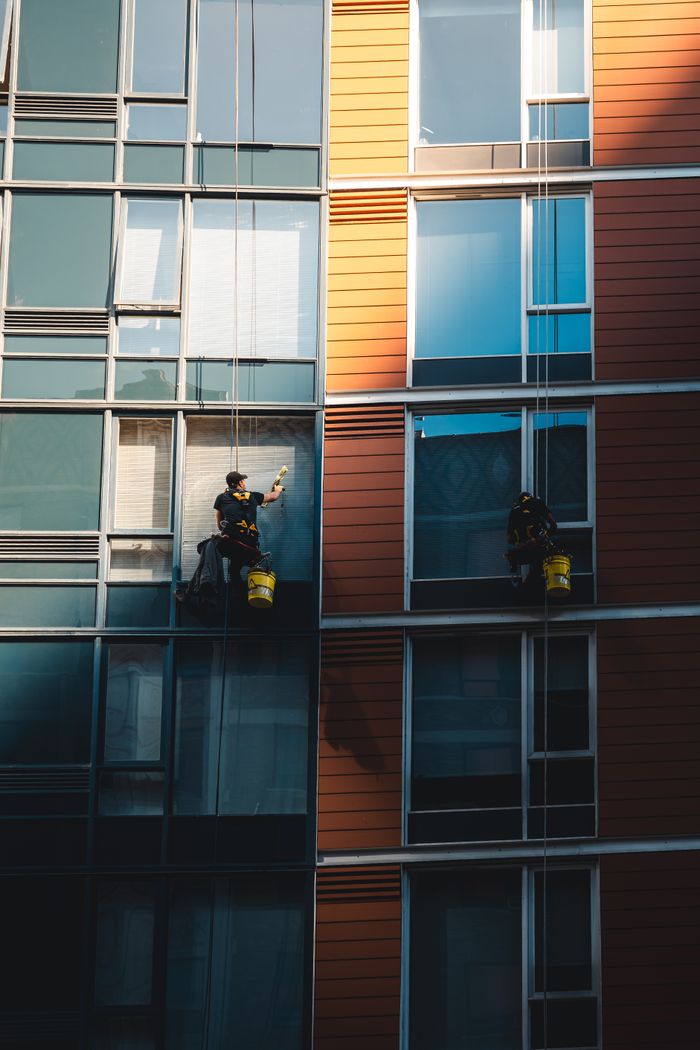 Two workers hanging to clean windows on a modern skyscraper facade.